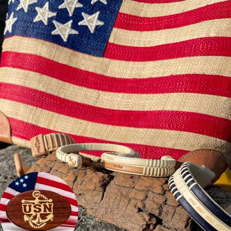 american flag behind bracelets balanced on a piece of driftwood and hithc cover in the bottom corner