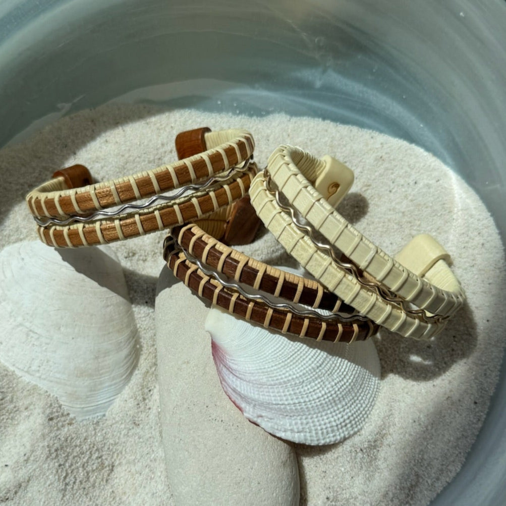 bracelets of wood and silver and gold fill in a glass bowl with sand and shells
