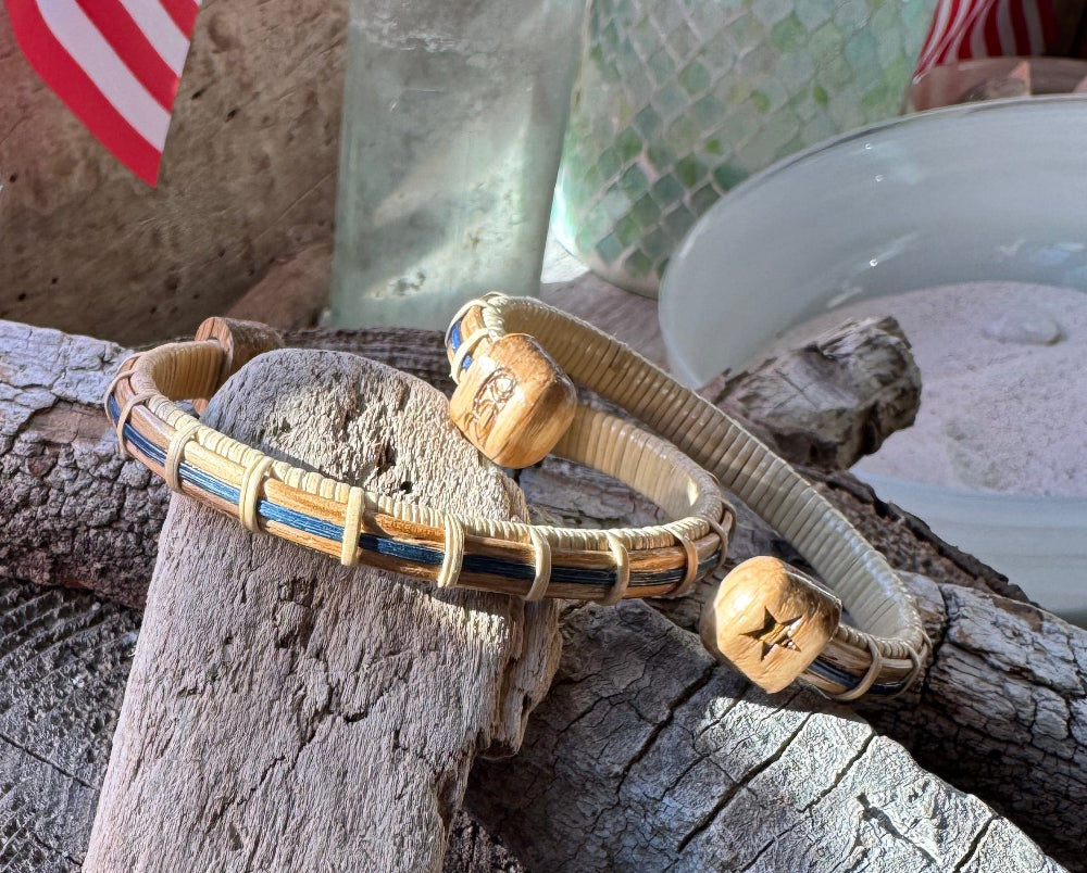 two cuff bracelets with 250 on one end cap and a star on the other balanced on wood and in front of a glass bowl and american flag