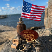 collection of jewelry and hitch cover on a rock ith woden jar and American flag behind them