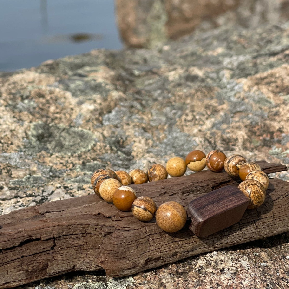 A stone bracelet with wooden beads displayed on a rock with a background of a dock and boats.