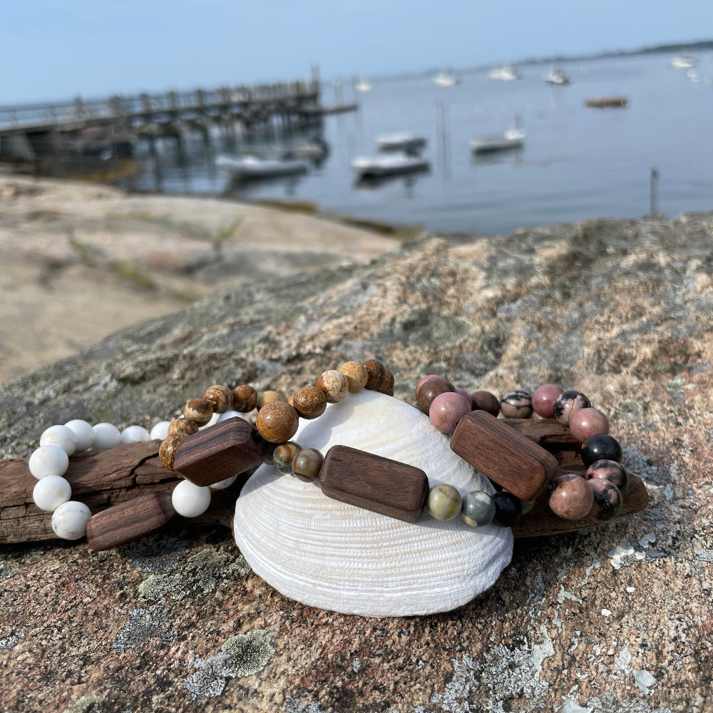 A stone bracelet with wooden beads displayed on a rock with a background of a dock and boats.