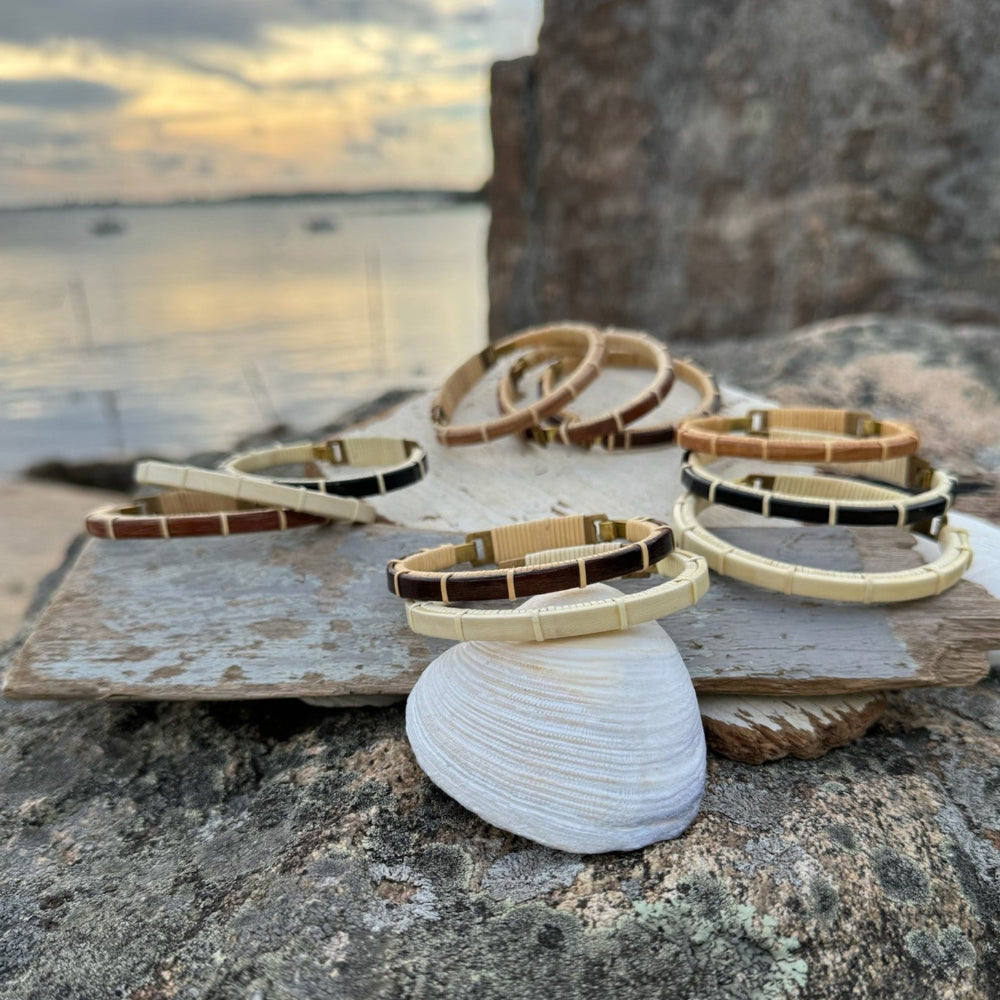 A series of cuff bracelets with clasp details, displayed on a flat surface near a body of water, showcasing various designs with wood and metal components.