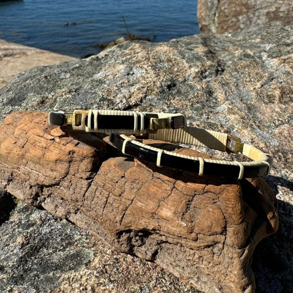 two bracelets balanced on driftwood and a rock in front of the ocean