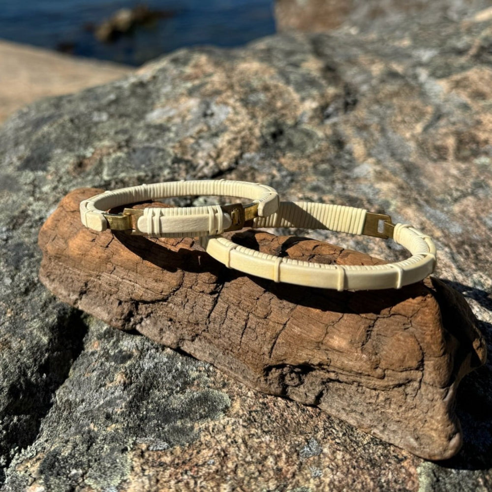 two cuff bracelets with clasp details, displayed on a flat surface near a body of water, showcasing various designs with wood and metal components.