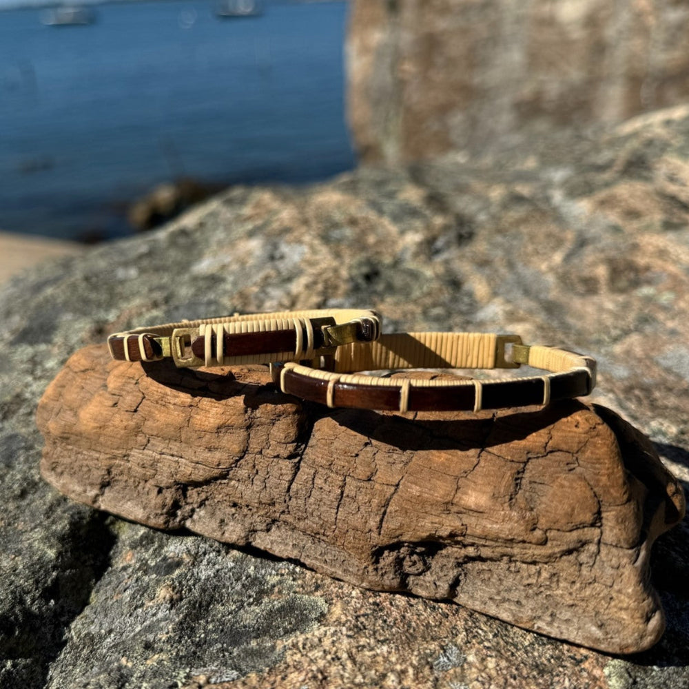 A series of cuff bracelets with clasp details, displayed on a flat surface near a body of water, showcasing various designs with wood and metal components.