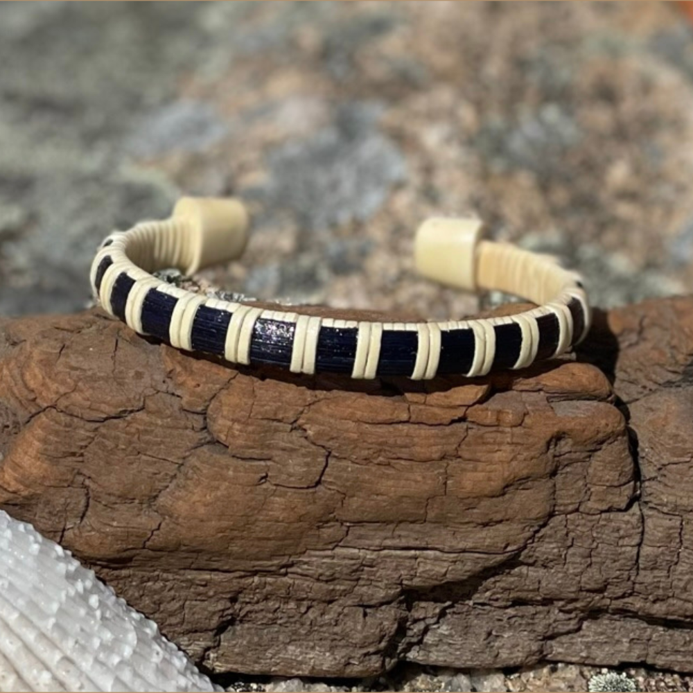 A wooden cuff bracelet with black and white patterned inlays, displayed on a natural stone surface.