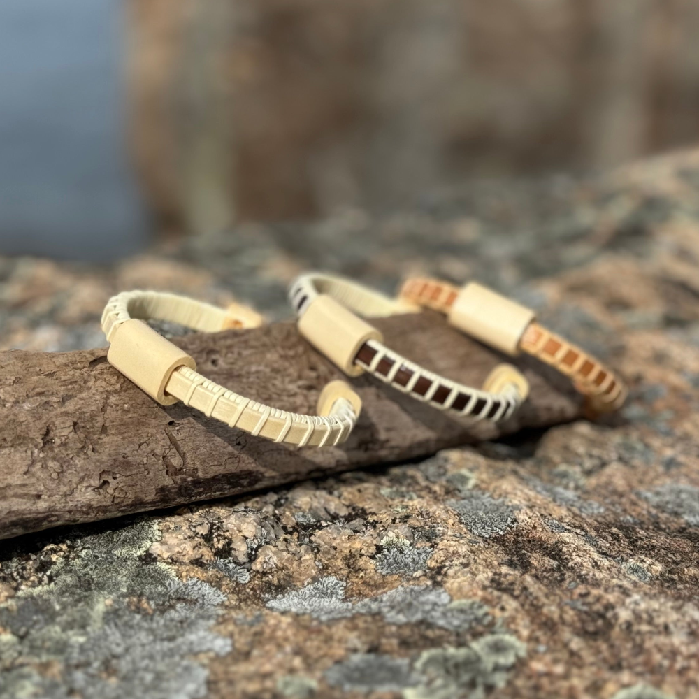Two cuff bracelets made of wood, one with a solid pattern and the other featuring a woven design, displayed on a rock.