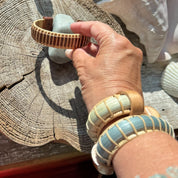 Two woven Harbor Mist cuff bracelets on a writ while the hand holds another woven bracelet by Stonington Designs