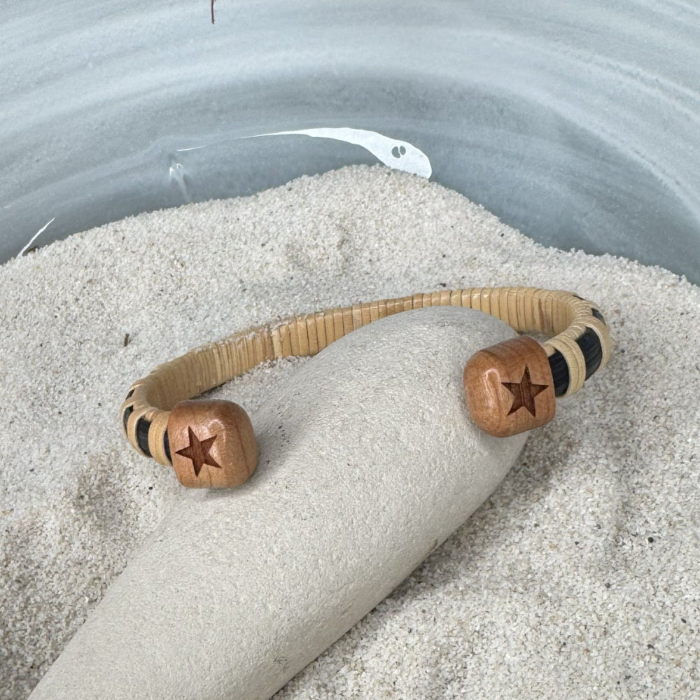 back side of cuff bracelet with star on each end, blaneced on a rock in a bowl of sand