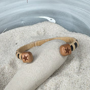 back side of cuff bracelet with star on each end, blaneced on a rock in a bowl of sand