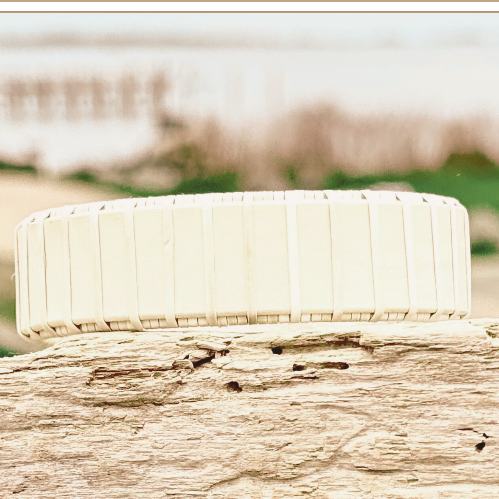 A two-tone cuff bracelet made of wood and metal, displayed on a sandy beach with a pier in the background.