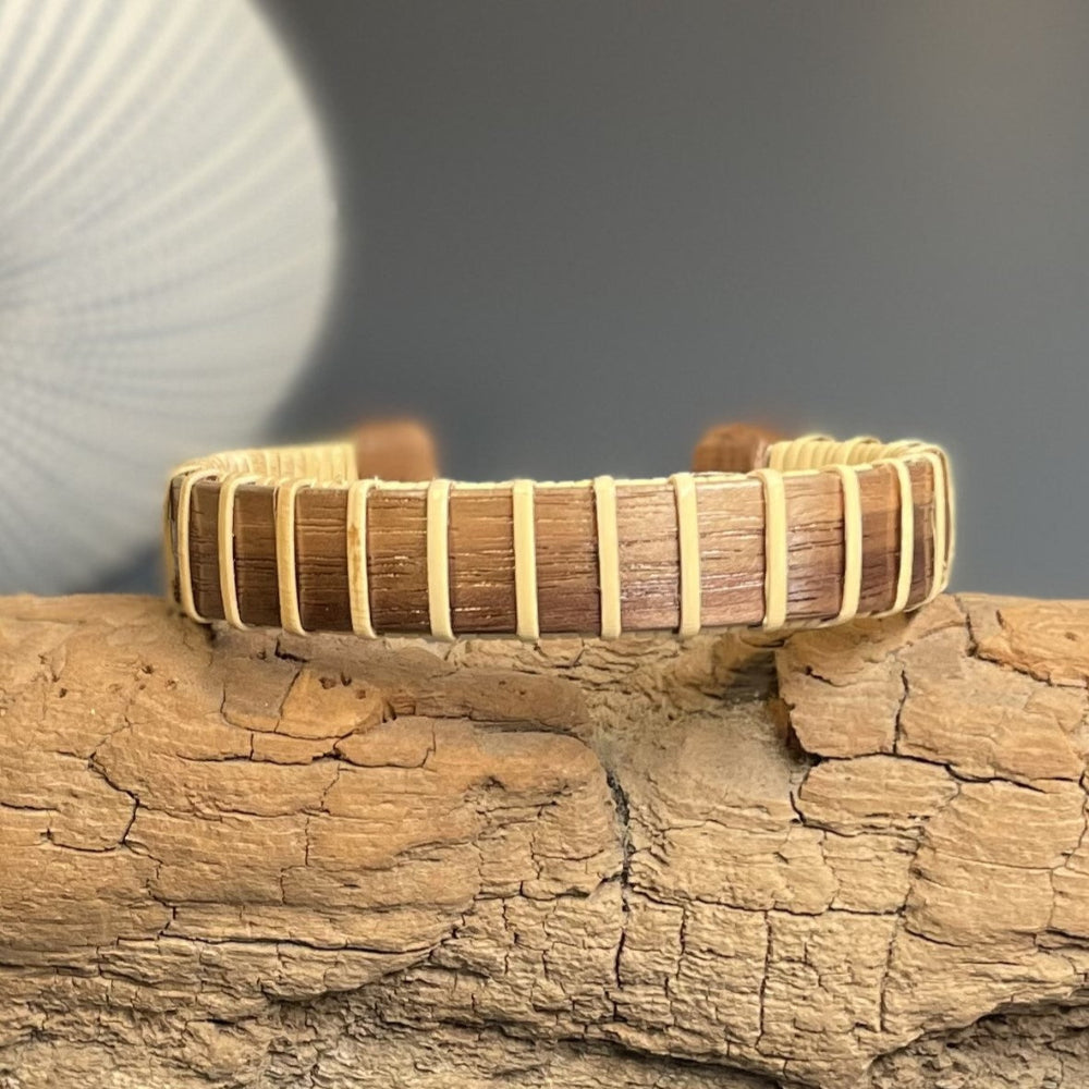 A wooden cuff bracelet with beige straps and a patterned design, displayed on a textured wooden surface.