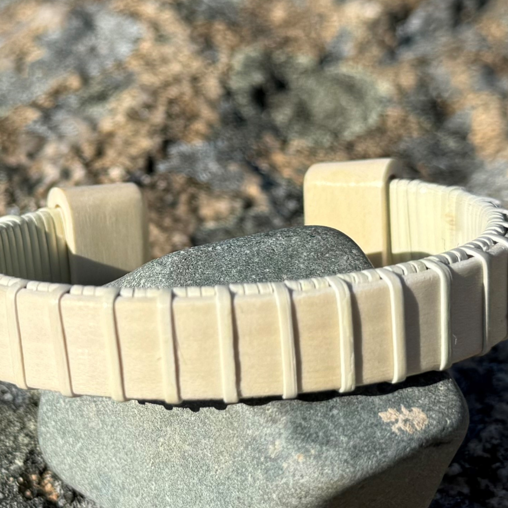 A wooden cuff bracelet with beige straps and a patterned design, displayed on a textured wooden surface.
