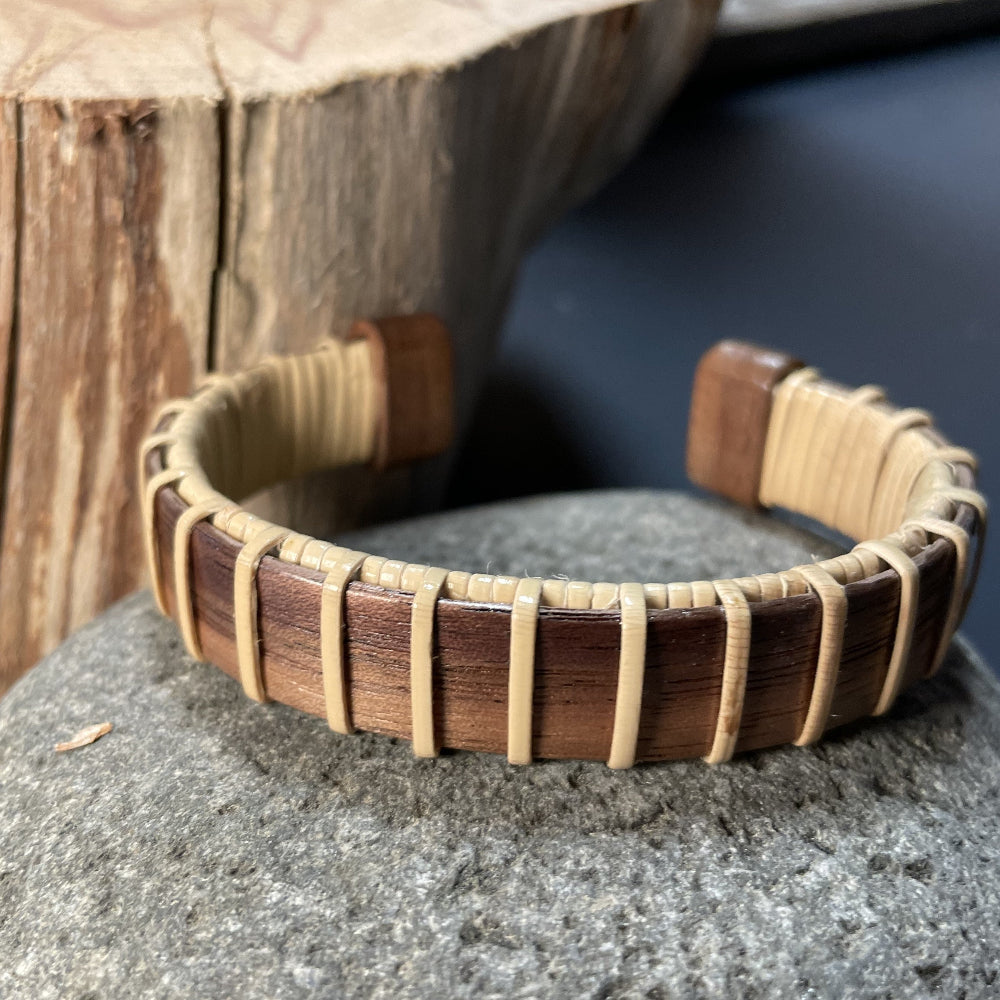 A wooden cuff bracelet with beige straps and a patterned design, displayed on a textured wooden surface.