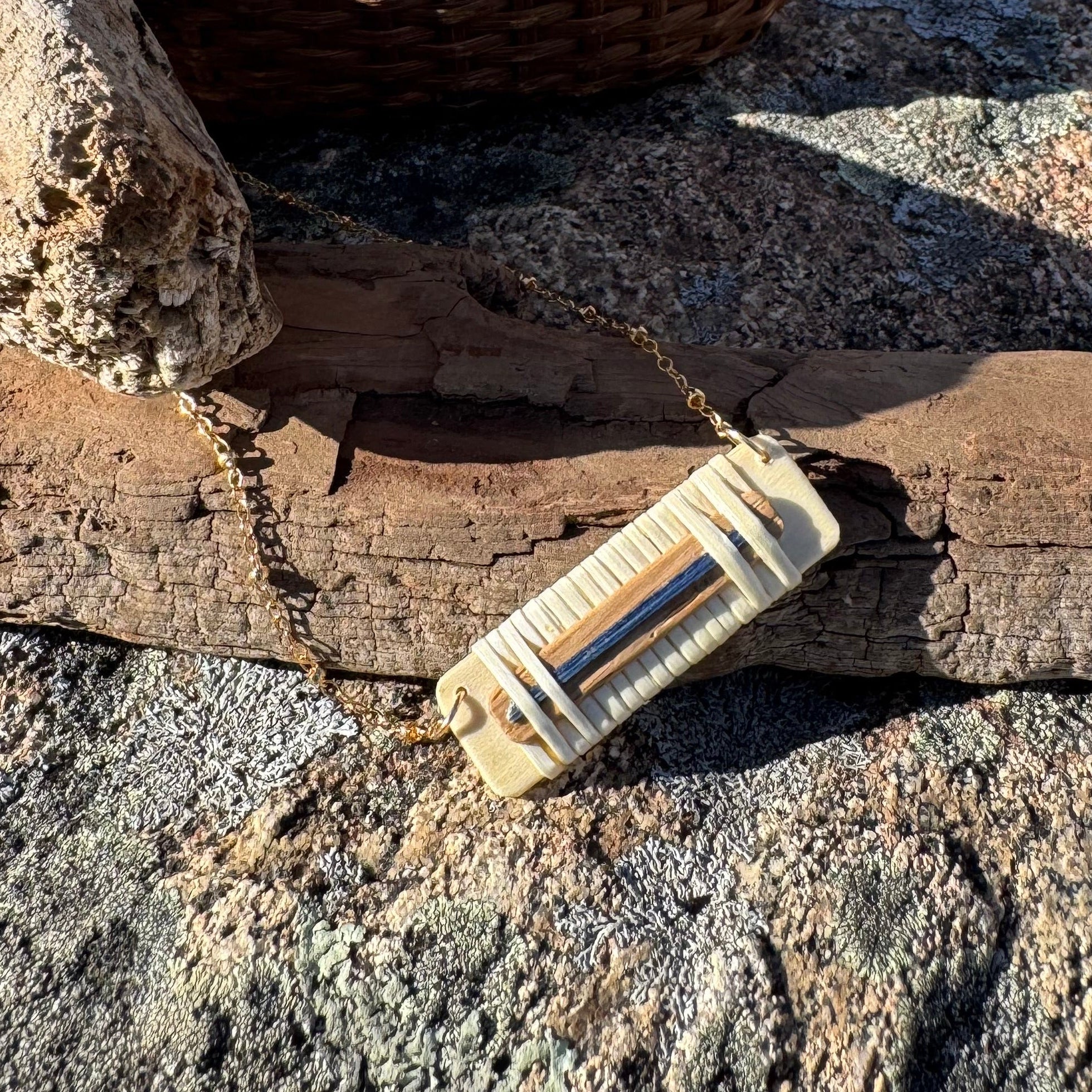 Woven necklace on a chain on edge of driftwoodwith basket in background