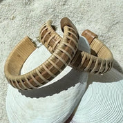 Close-up of handcrafted cherry wood large hoop earrings with woven natural weaver accents and secure post backing, resting on a shell.