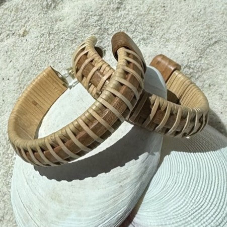Close-up of handcrafted cherry wood large hoop earrings with woven natural weaver accents and secure post backing, resting on a shell.