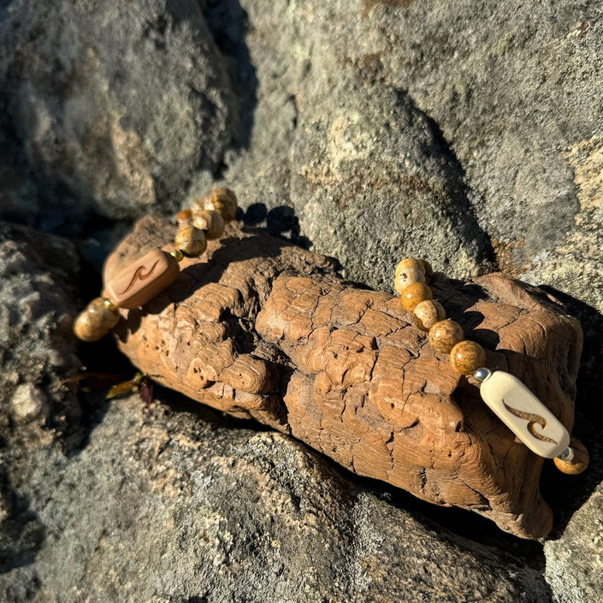 A wooden bracelet with etched wave patterns and stone beads, displayed on a rocky surface.