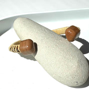 Cherry wood handcrafted cuff from Drift by Stonington Designs, showing woven end caps on a smooth beach stone.