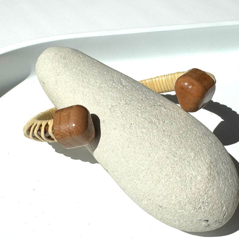 Cherry wood handcrafted cuff from Drift by Stonington Designs, showing woven end caps on a smooth beach stone.