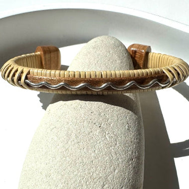 Drift by Stonington Designs handcrafted cuff in cherry wood with a sterling silver wave accent, displayed on a natural stone.