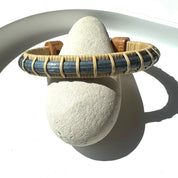Estuary cuff bracelet from the Marsh Collection, slim hand-dyed blue bamboo with hand-carved cherry end caps, displayed on a natural stone.
