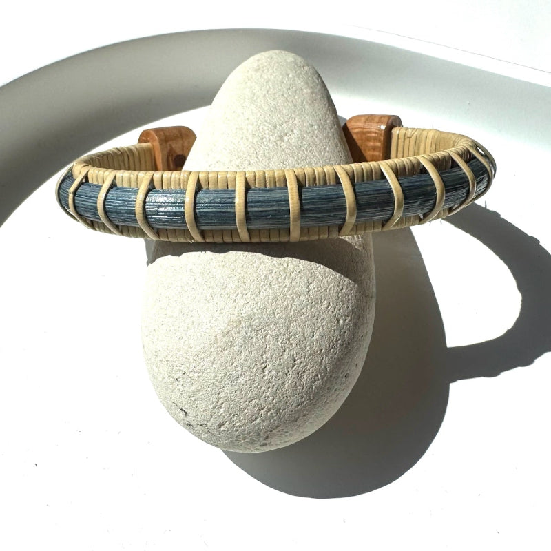 Estuary cuff bracelet from the Marsh Collection, slim hand-dyed blue bamboo with hand-carved cherry end caps, displayed on a natural stone.