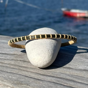 Handcrafted Forrest dark green hand-dyed bamboo cane Secrets bangle bracelet resting on a beach stone with a fishing boat on the water in the background — handmade by Military Spouse artisans in Stonington, Connecticut using American-made materials.