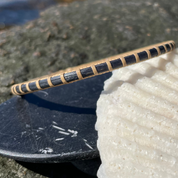 Handcrafted Ocean deep blue hand-dyed bamboo cane Secrets bangle bracelet resting on rocks beside a seashell — handmade by Military Spouse artisans in Stonington, Connecticut using American-made materials.