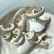 Several pairs of handcrafted medium hoop earrings with blue and sea glass woven detail and light weaver, scattered in sand.