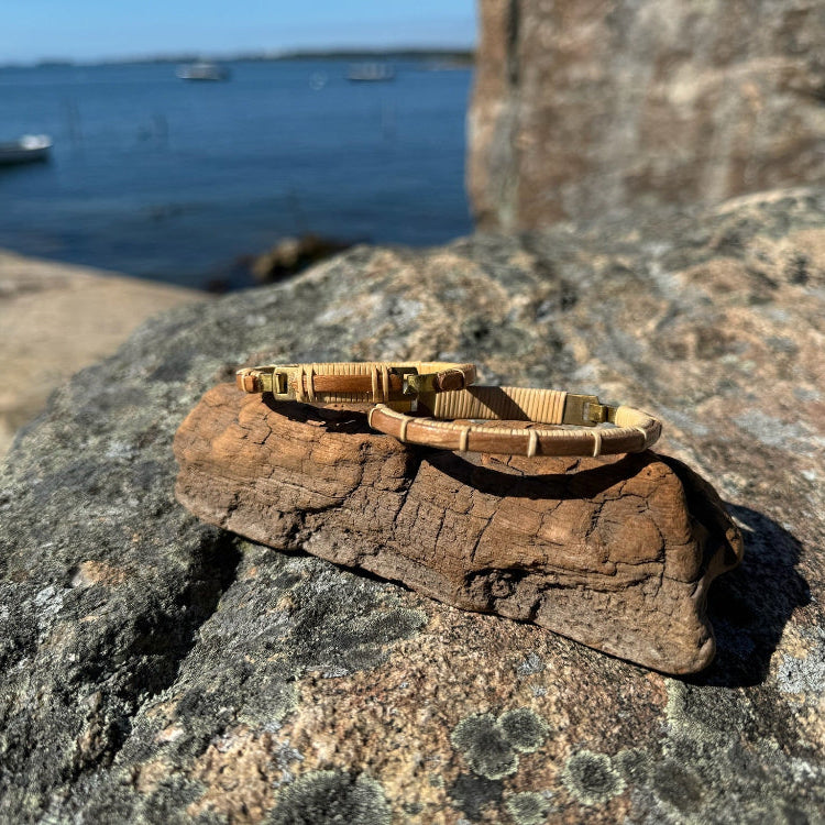 Single cherry Breakers clasp bracelet resting on driftwood on granite rocks with a harbor and blue sky in the background.