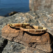 Two cherry Breakers clasp bracelets resting on driftwood on granite rocks with a harbor and blue sky in the background.