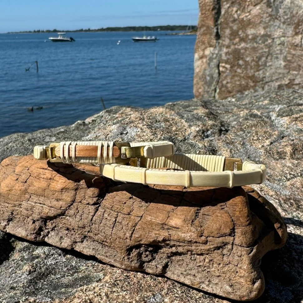 Single cherry-holly Breakers clasp bracelet resting on driftwood on granite rocks with a harbor in the background.