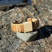 Handcrafted cherry Island Cuff Bracelet with holly slider bead balanced on a smooth stone on coastal rocks in sunlight