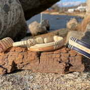 Handcrafted cherry Our Love Runs Deep Etched Double Cuff Bracelet displayed on driftwood alongside other Stonington Designs submarine-themed bracelets, with coastal rocks and water in the background.