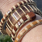 Four Clubhouse cuff bracelets in cherry, holly, rosewood, and walnut stacked on a wrist, showing the open-weave cane texture and wood grain detail.