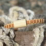 Single cherry Cove cuff bracelet with holly slider resting on nautical rope on granite rocks.