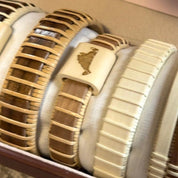 Handcrafted cherry wood cuff bracelet with an etched Martha's Vineyard shape on a holly wood slider bead, displayed in a row alongside other bracelets in a jewelry box.