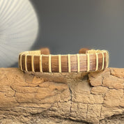Handcrafted cherry Maverick Cuff Bracelet resting on driftwood with a seashell in the background, showing the wide cherry wood stave and holly weave construction.