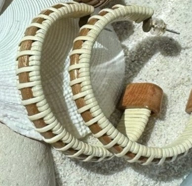 Close-up of handcrafted cherry wood large hoop earrings with woven cream accents and secure post backing, resting on a shell.