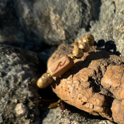 Close-up of a handcrafted Slivers wave bracelet with an etched cherry wood bead and picture jasper stone beads, resting on a rock.