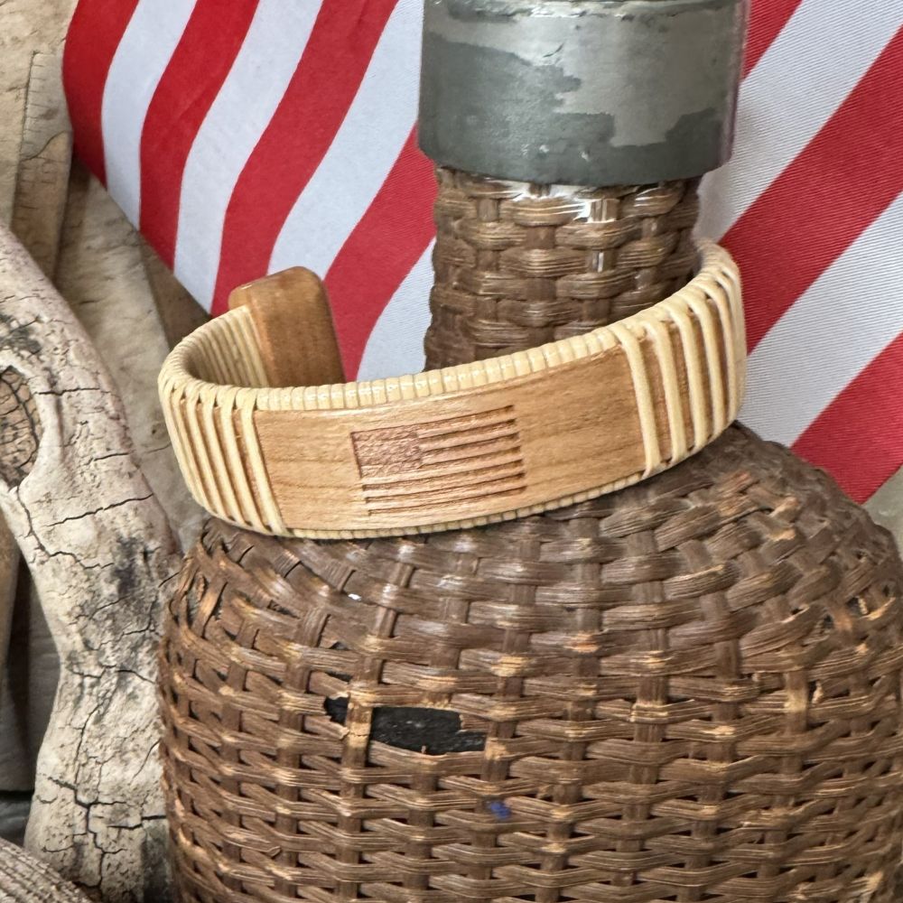 Handcrafted cherry wood Star Spangled cuff bracelet with an etched American flag, resting on a woven basket against a red and white striped flag background.