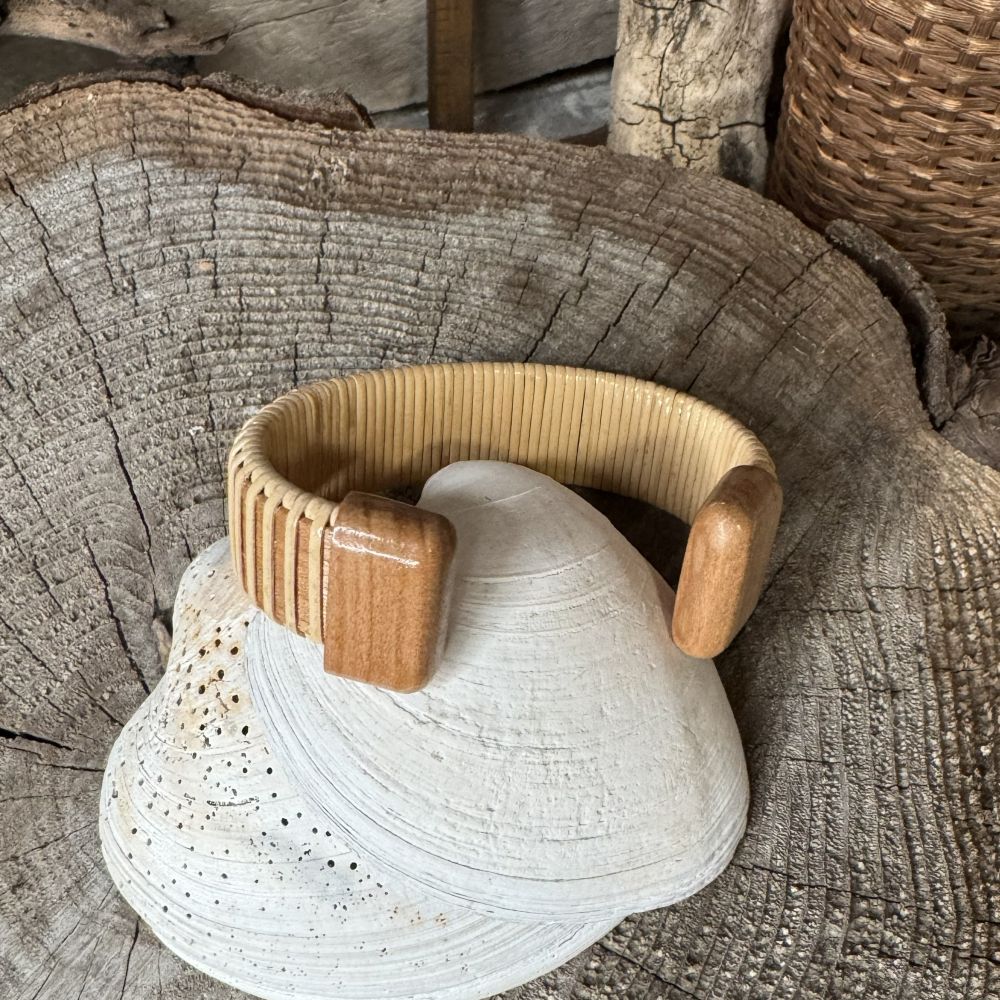 Handcrafted cherry wood Star Spangled cuff bracelet with an etched American flag end cap, balanced on a seashell with driftwood in the background.