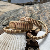 Three Clubhouse cuff bracelets in cherry, walnut, and rosewood stacked on seashells on granite rocks.