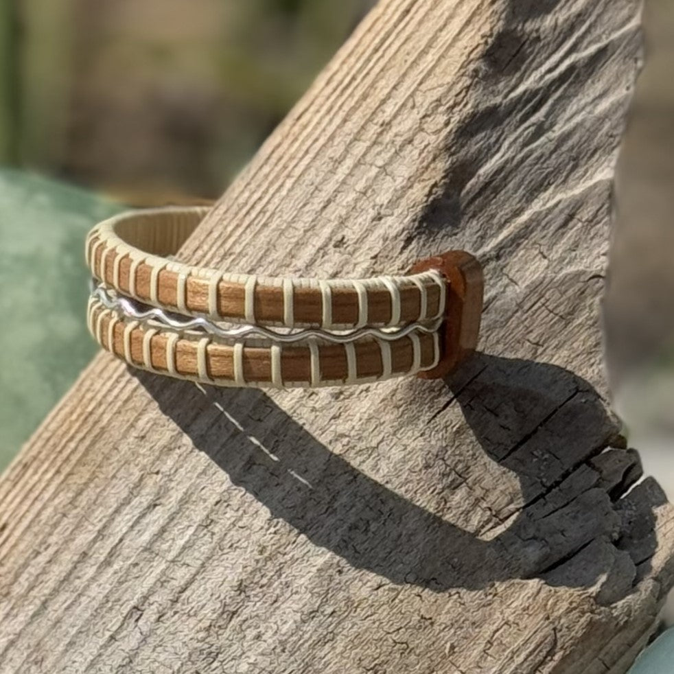 Close-up of a handcrafted cherry wood Waves triple cuff bracelet with a sterling silver accent band.