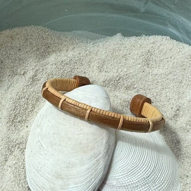 Handcrafted cherry wood Bannister cuff bracelet with open-weave light weaver detailing, displayed on shells and sea stones — handmade by Military Spouse artisans in Stonington, Connecticut using American-made materials.
