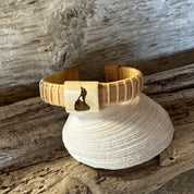 Handcrafted holly wood cuff bracelet with an etched Block Island shape on the center bead, balanced on a shell with driftwood in the background.