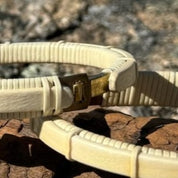 Close-up of two holly Breakers clasp bracelets showing the brass clasp detail, resting on driftwood outdoors.