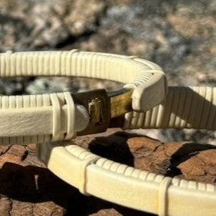 Close-up of two holly Breakers clasp bracelets showing the brass clasp detail, resting on driftwood outdoors.